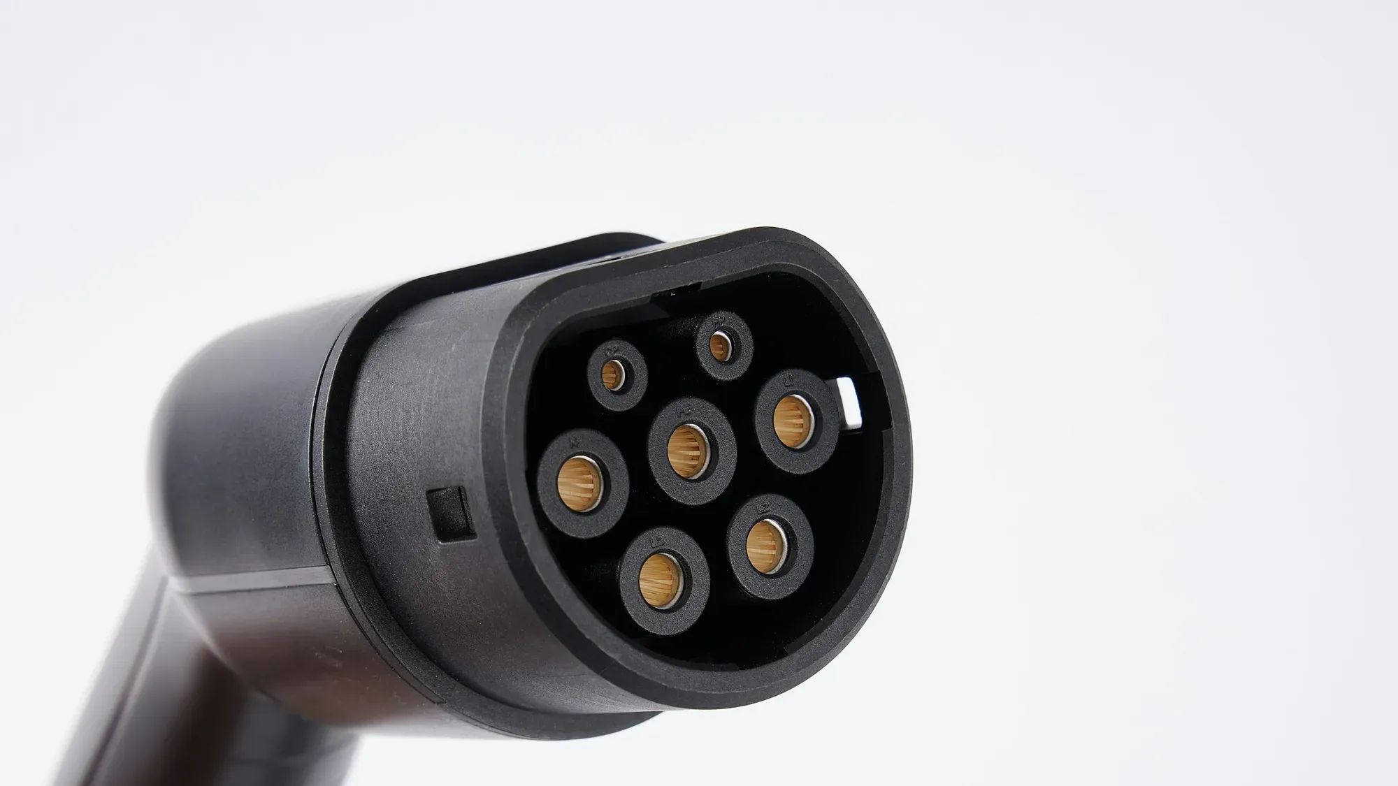 Primer plano de un conector de carga Tipo 2 para carro eléctrico, con siete pines, sobre fondo blanco