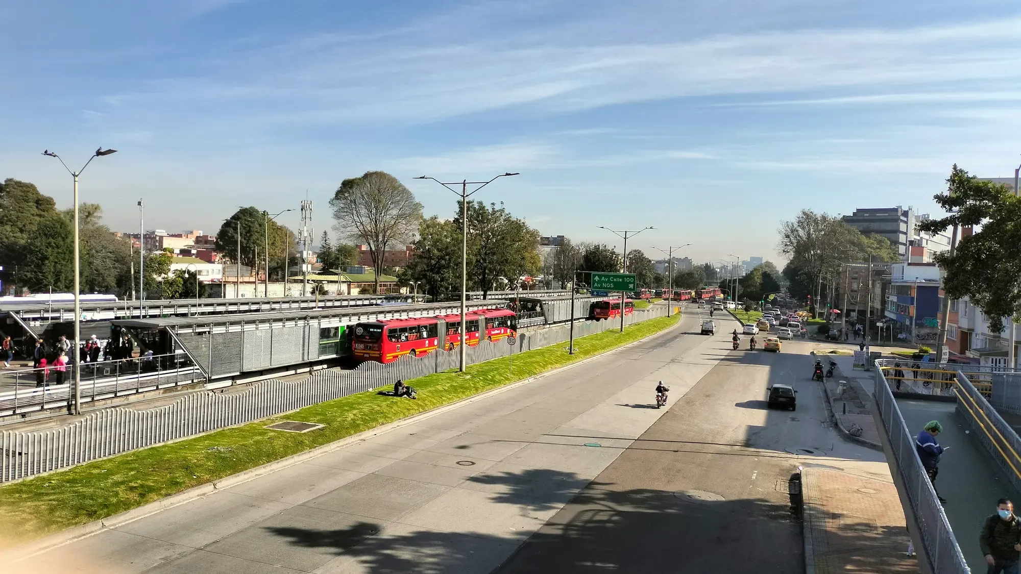 Corredor vial de Bogotá con un bus articulado, carriles mixtos y árboles a los lados