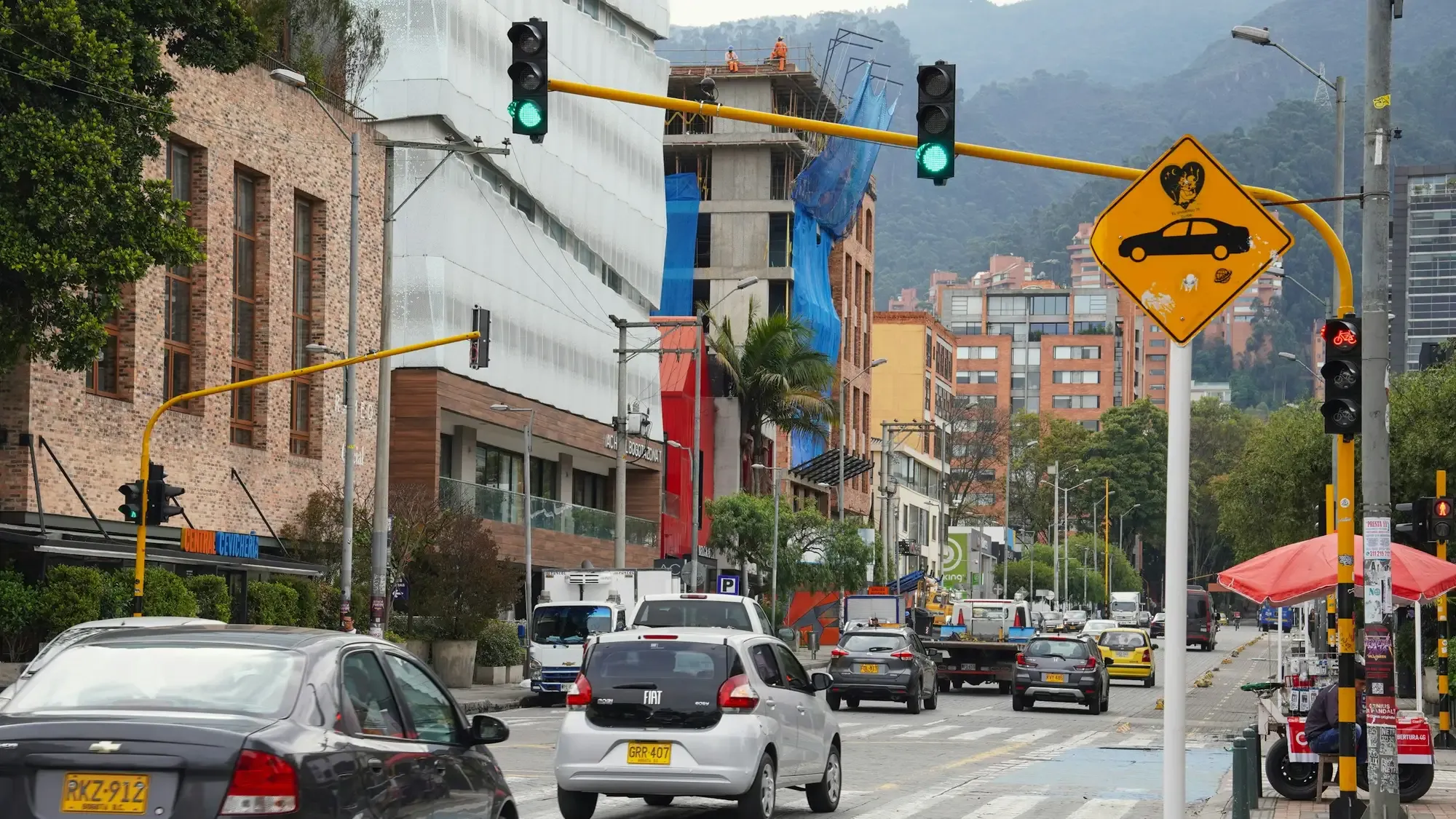 Carros particulares detenidos en una calle de Bogotá con semáforos y edificios de ladrillo